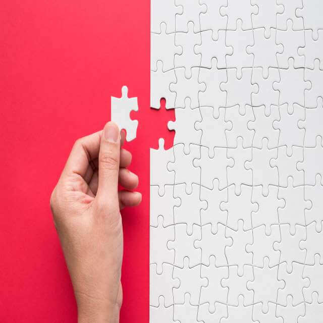 Hand putting the last piece of white jigsaw puzzle on red background and place for your content